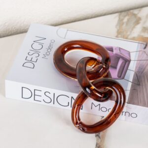 a modern abstract chain-link decorative sculpture made from glass or resin. Its interlocking rings and amber tone make it a stylish accent often used for coffee tables, trays, and bookshelf styling in contemporary interiors.