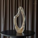 a striking decorative sculpture designed to elevate contemporary interiors. Featuring a smooth flowing silhouette and a transparent glass body filled with delicate gold accents, this artistic piece brings sophistication and visual interest to any room.